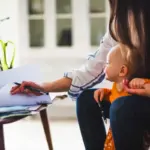 Midsection of working mother examining documents with baby girl at home office
