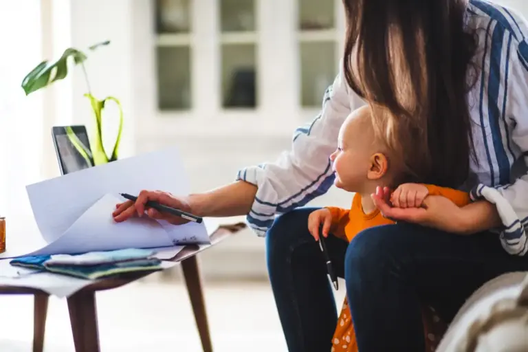 Midsection of working mother examining documents with baby girl at home office