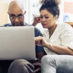 Couple looking at laptop while sitting on sofa at home